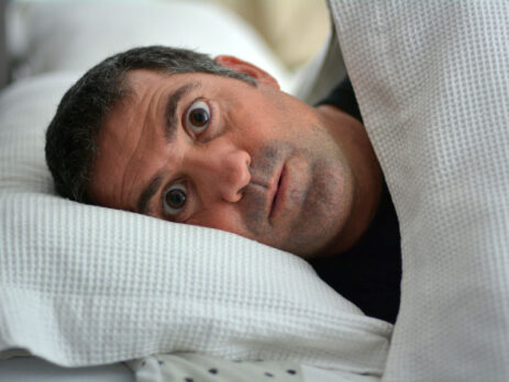 Wide-eyed man laying in bed unable to sleep due to a nightmare