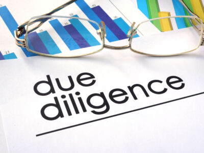 Due diligence reports and charts laying on a desk with a pair of glasses